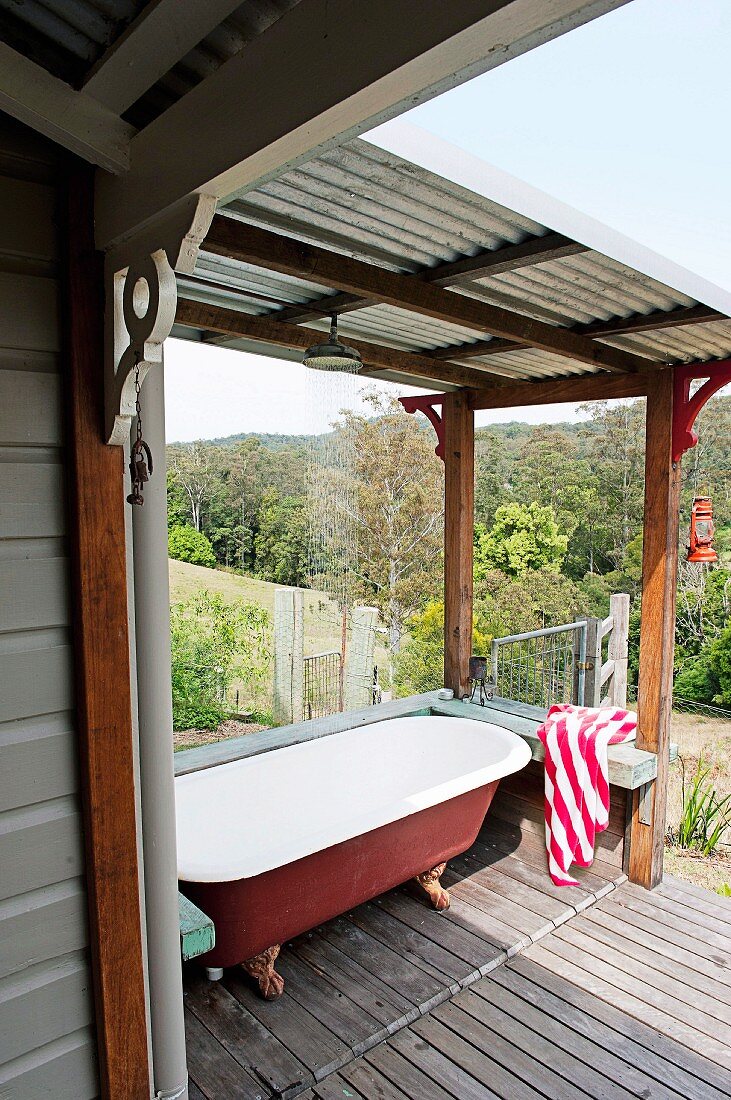 Vintage bathtub on wooden floor of roofed terrace and view across Mediterranean landscape