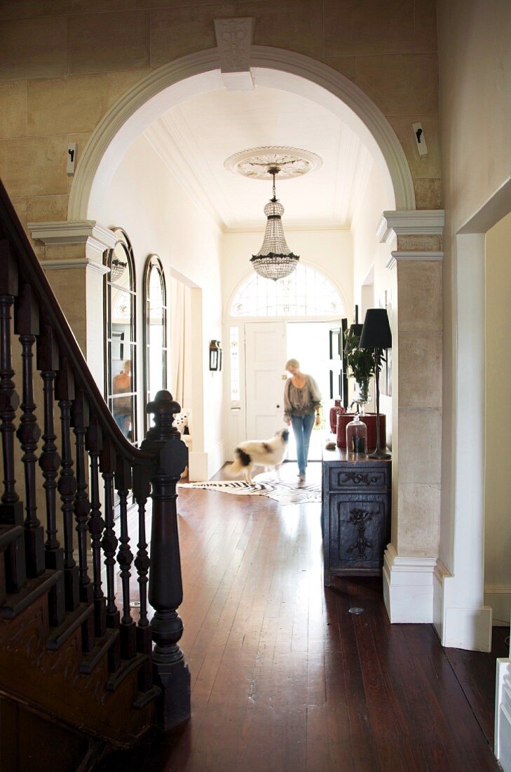 View from stairwell through archway of woman and dog in narrow hallway in grand villa