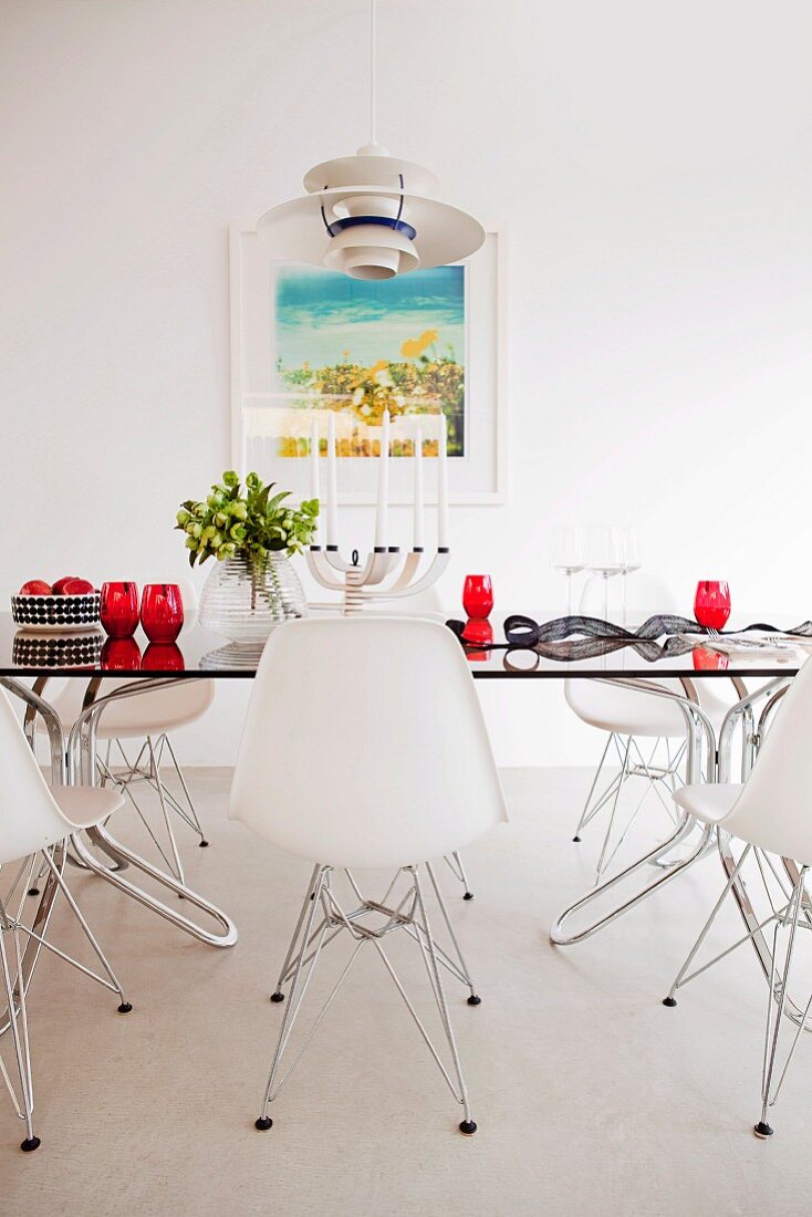 Klassiker Schalenstühle in Weiß um Glastisch mit roten Trinkgläsern in minimalistischem Esszimmer
