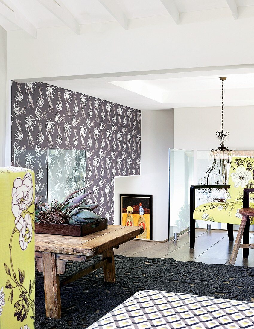 Florale Muster auf Wandtapete, gelbgrünen Polsterstoffen und im dunkelgrauen Strukturteppich des Studios in einem Wohnhaus; Kronleuchter über Treppe im Hintergrund