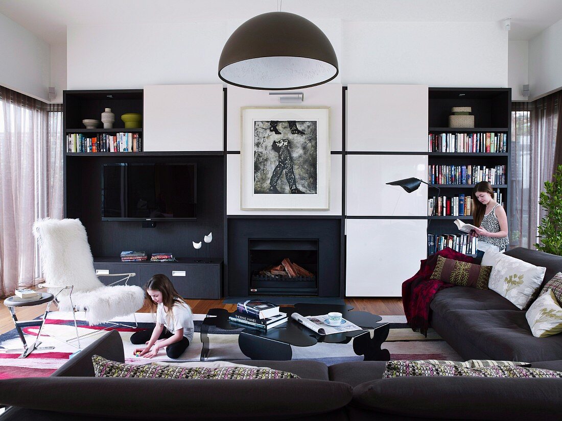 Kinder in modernem Wohnzimmer mit schwarzem Sofa übereck und offener Kamin