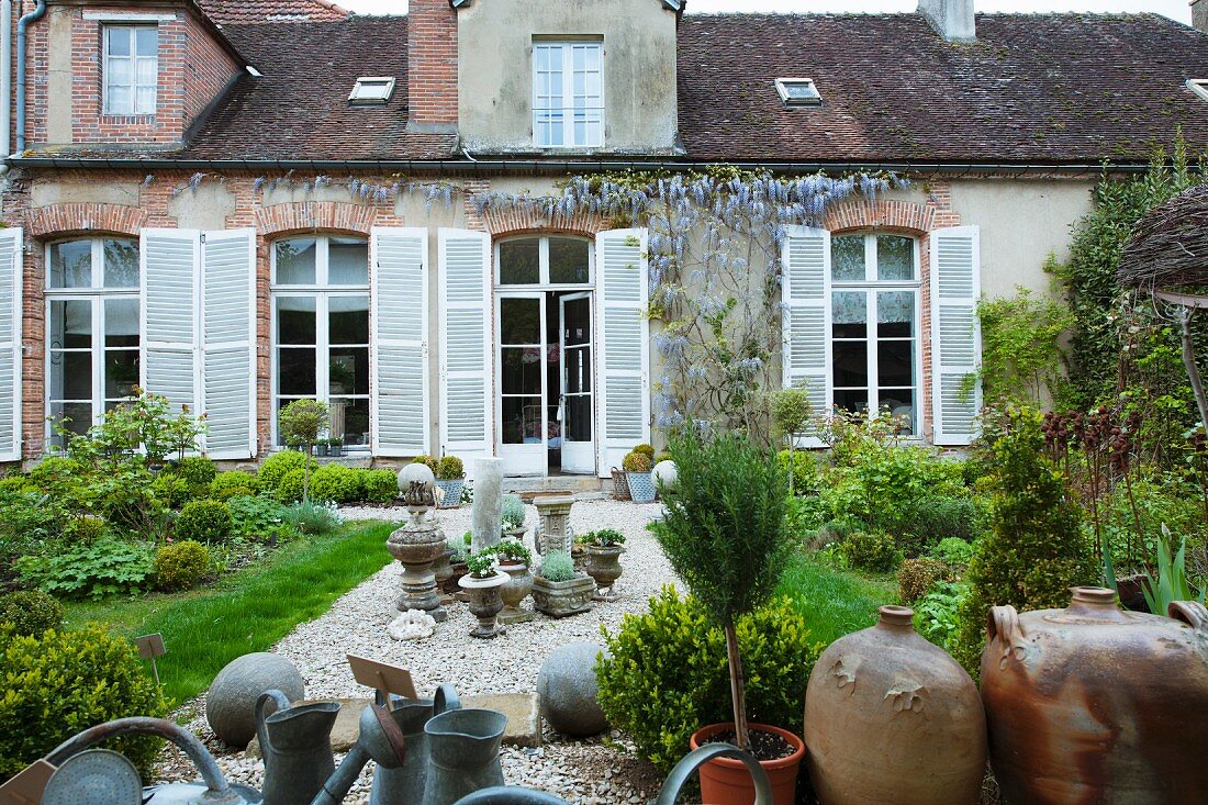 Zum Verkauf stehende Kannen, Stein- und Tongefässe auf Kiesweg im Garten eines alten, französischen Landhauses