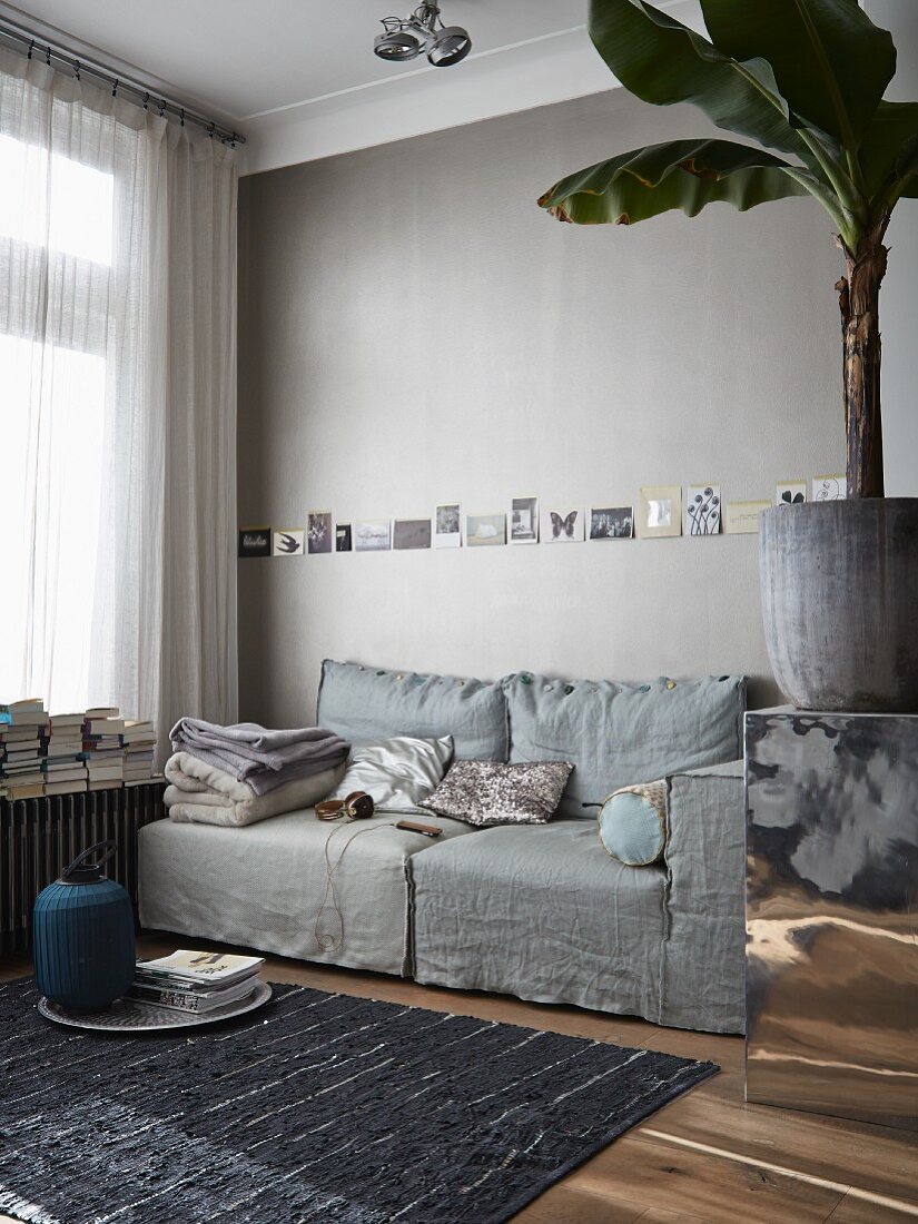 Living room in warm shades of grey with row of postcards tacked on wall above comfortable sofa