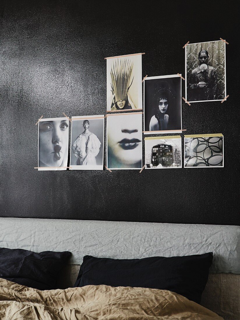Bed with upholstered headboard below photos tacked to black-painted wall