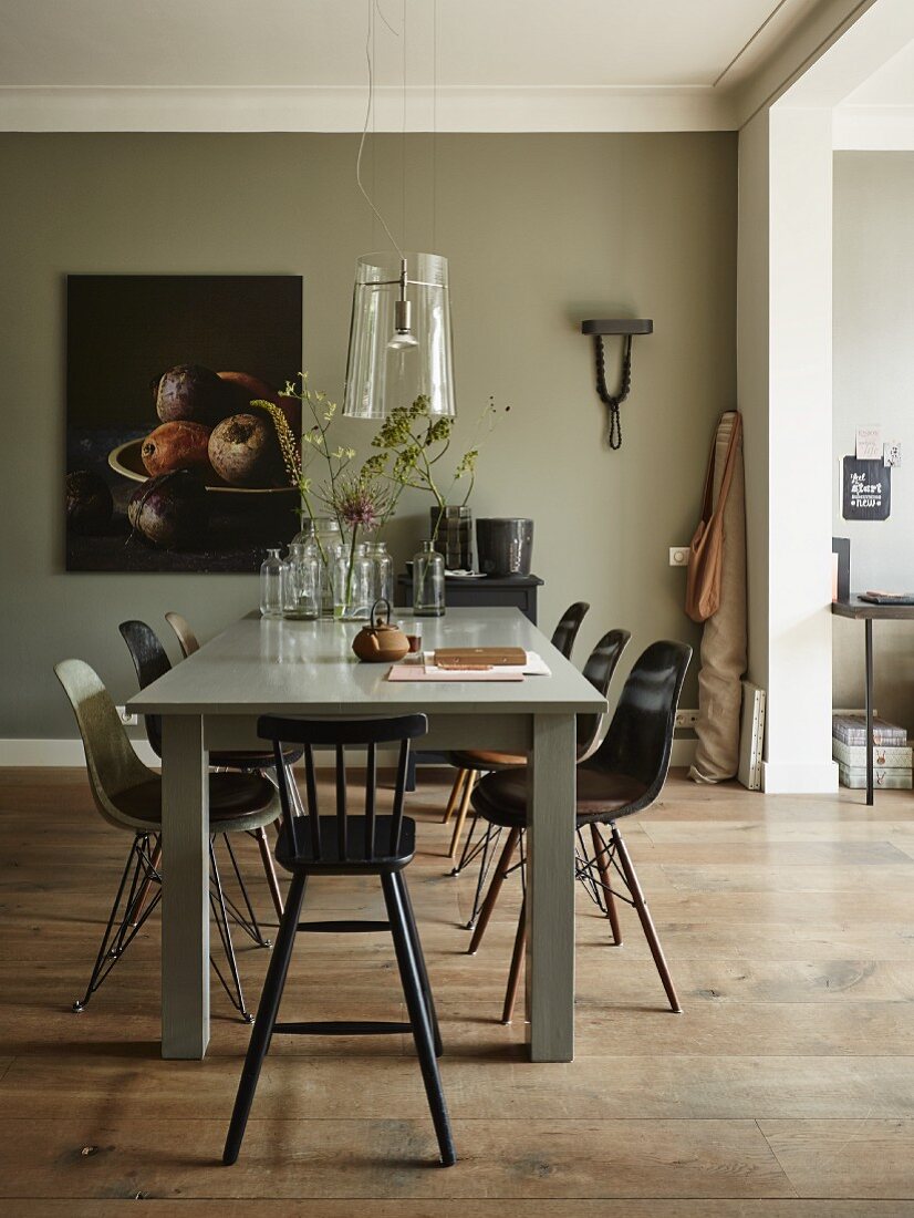 Essplatz mit Eames Stühlen und Kinderhocker an grau lackiertem Tisch mit Glasschirm-Leuchte; Stillleben an der Wand im Hintergrund