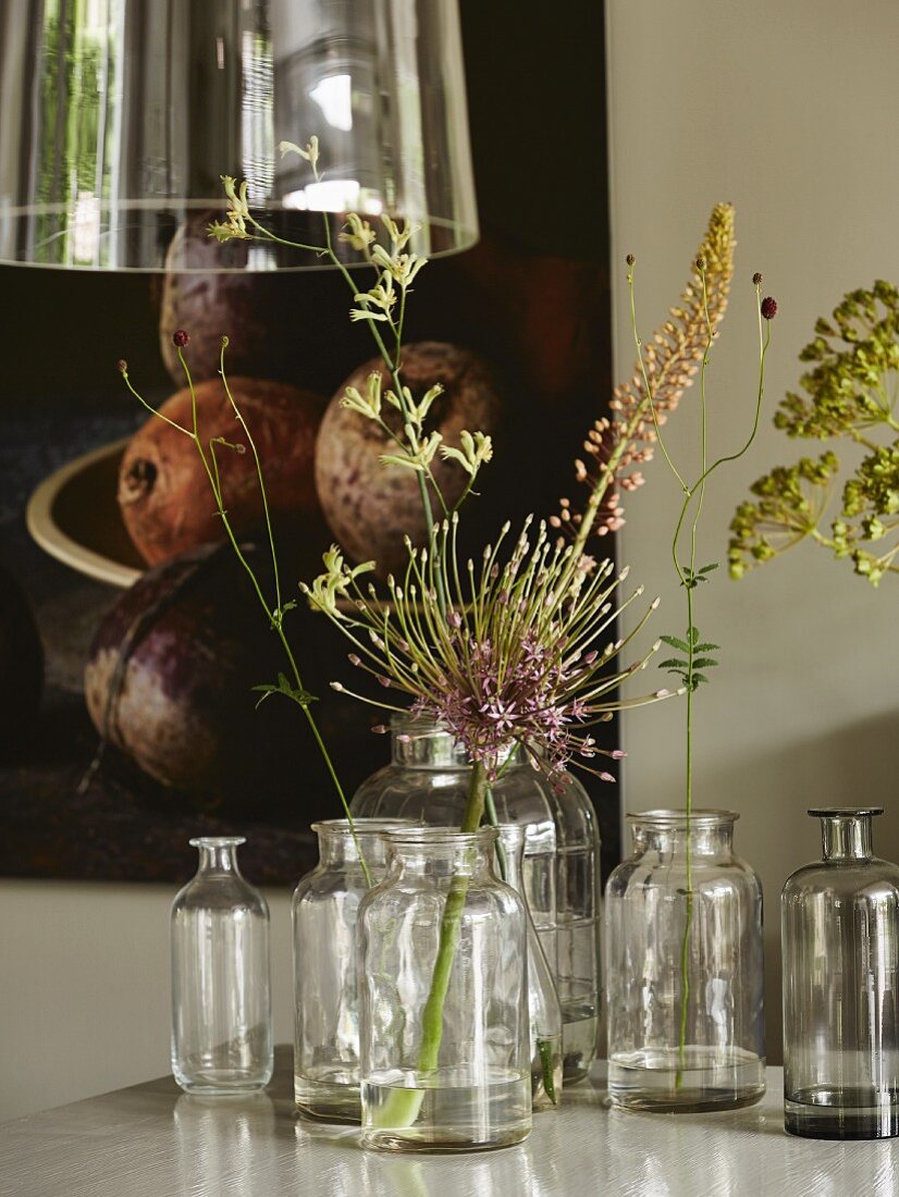 Alte Glasflaschen mit einzelnen Blütenstengeln auf Esstisch, darüber Hängeleuchte mit Glasschirm