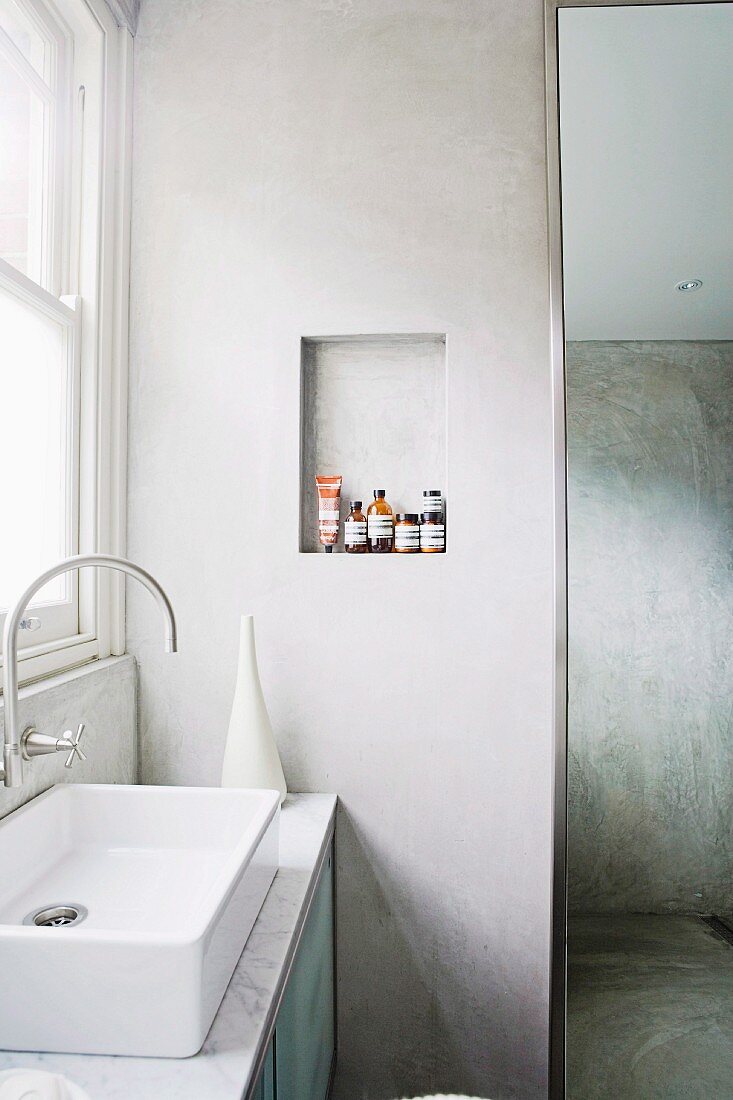Waschtisch mit Designer Armatur am Fenster, neben Wand mit kleiner Nische und hohem Spiegel
