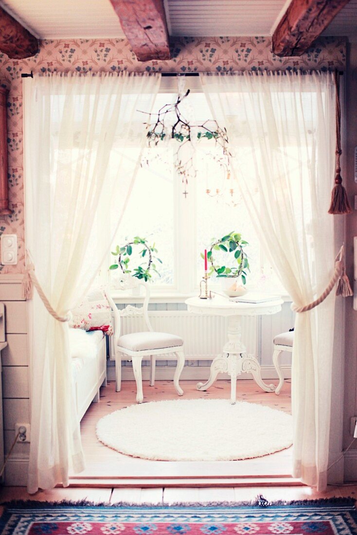 Sitzplatz mit weissen Stilmöbeln in einem dekoriertem Fenstererker, davor drapierten Vorhänge und aufgehängtem Mistelzweig