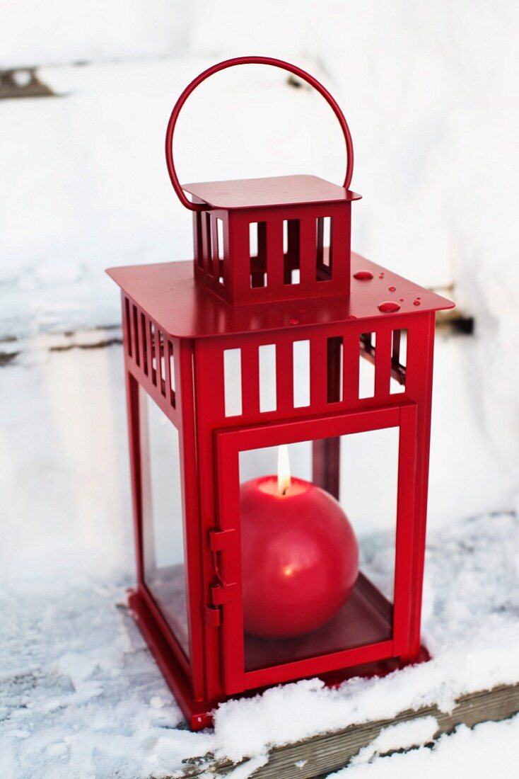Red, spherical candles in red lantern on snowy wooden steps