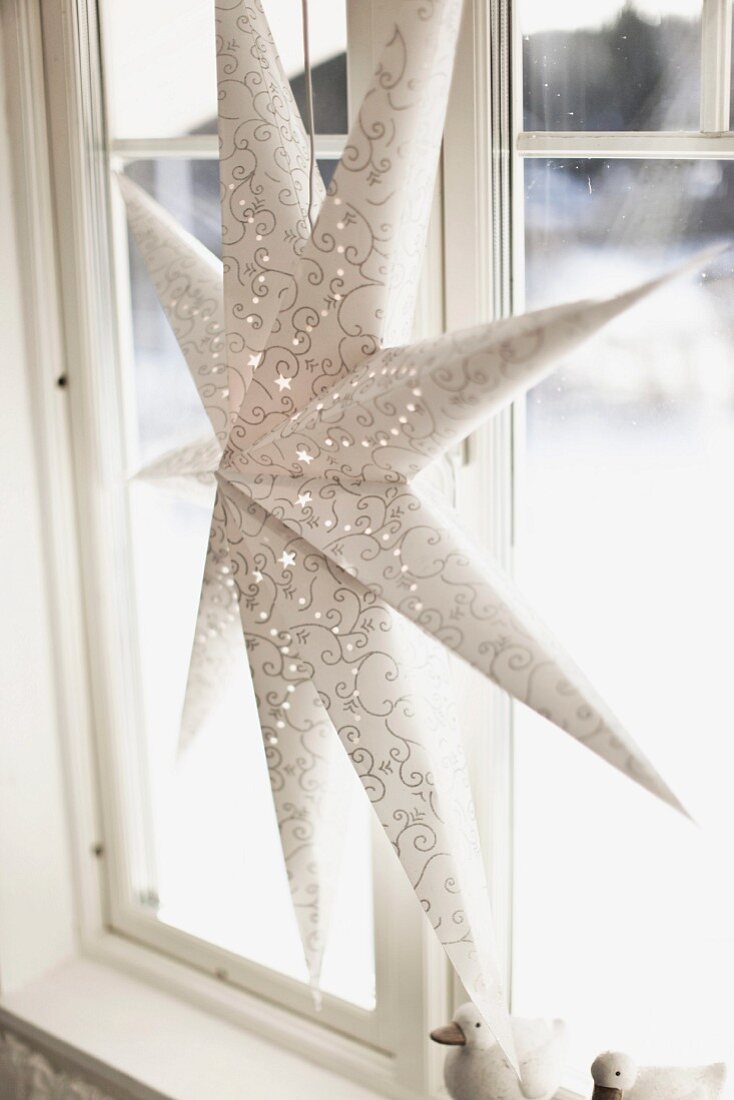White paper star lantern with delicate pattern of circles hanging from window frame