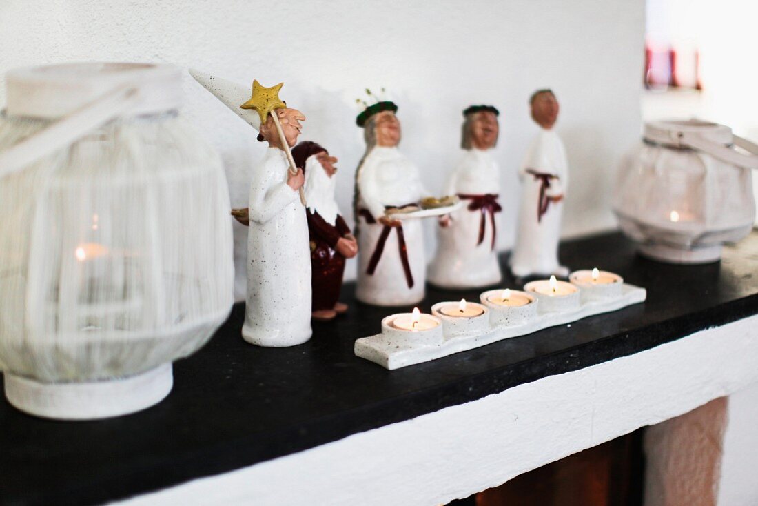 Carol singer figurines, tealights and candle lanterns arranged on mantelpiece