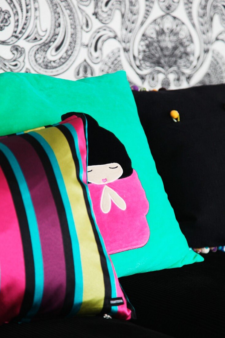Kissen mit Streifenbezug vor Kissen mit japanischem Motiv auf schwarzem Sofa