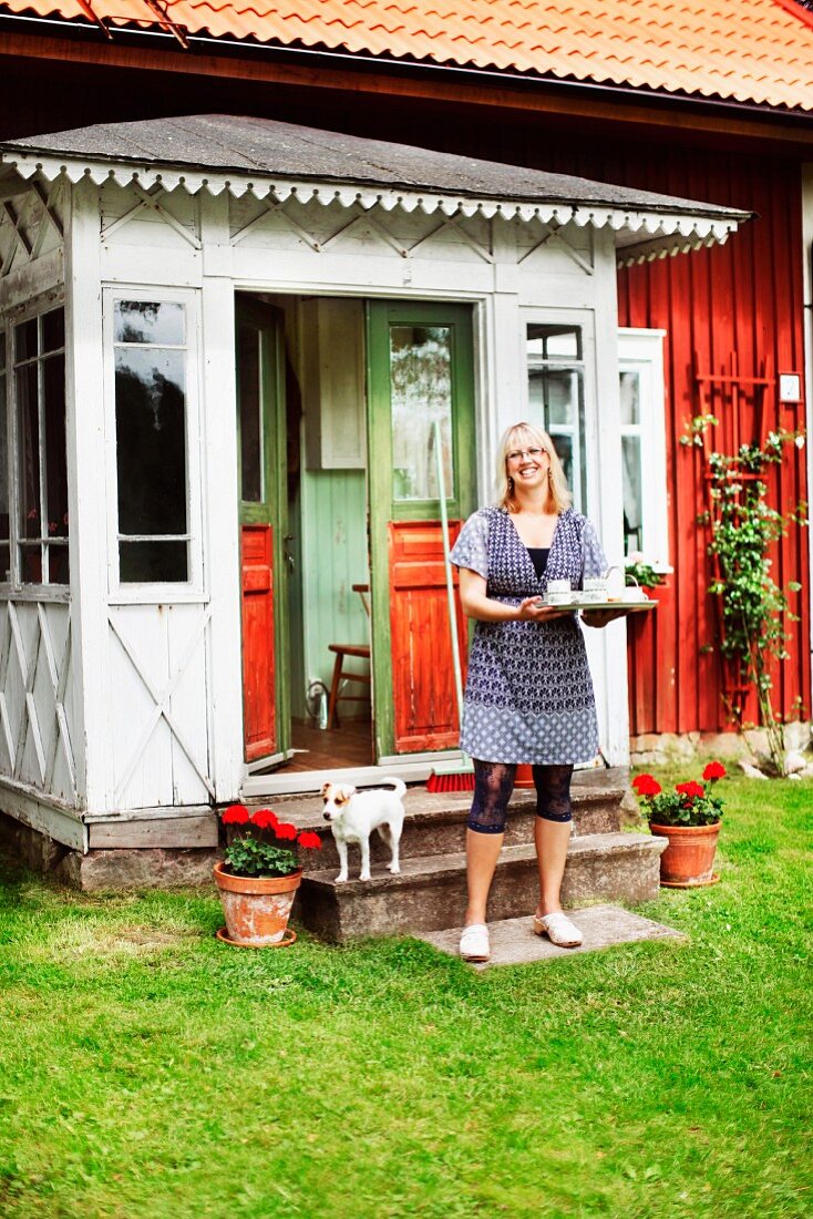 Lachende Frau mit Tablett vor dem Windfang eines schwedischen Holzhauses