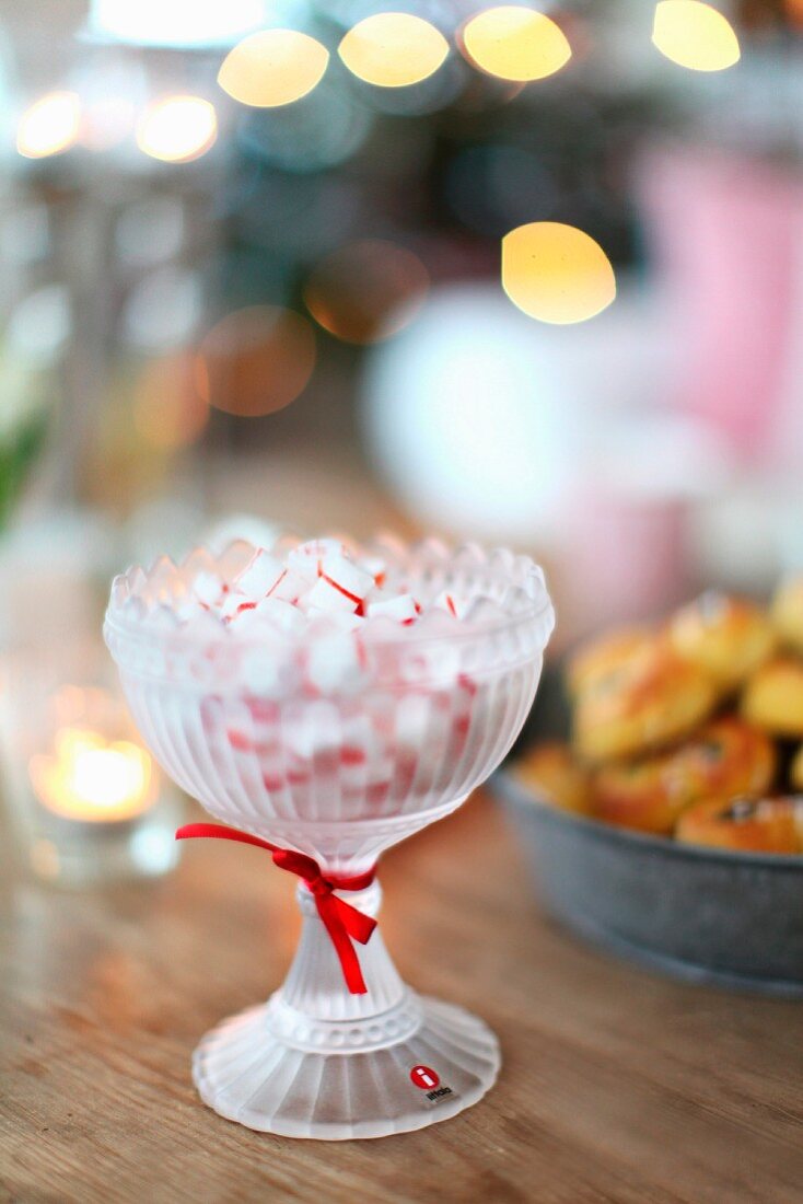 Bonbons in Retro-Glasschale mit roter Schleife auf Holztisch