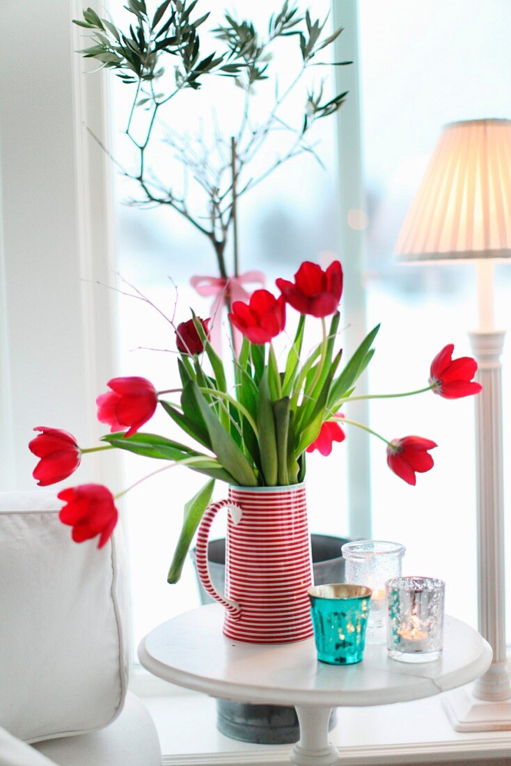 Roter Tulpenstrauss in rotweiss gestreiftem Krug auf Beistelltisch vor dem Fenster