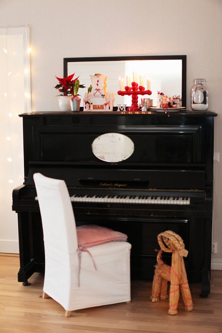 Straw figurine next to chair with white loose cover in front of black piano