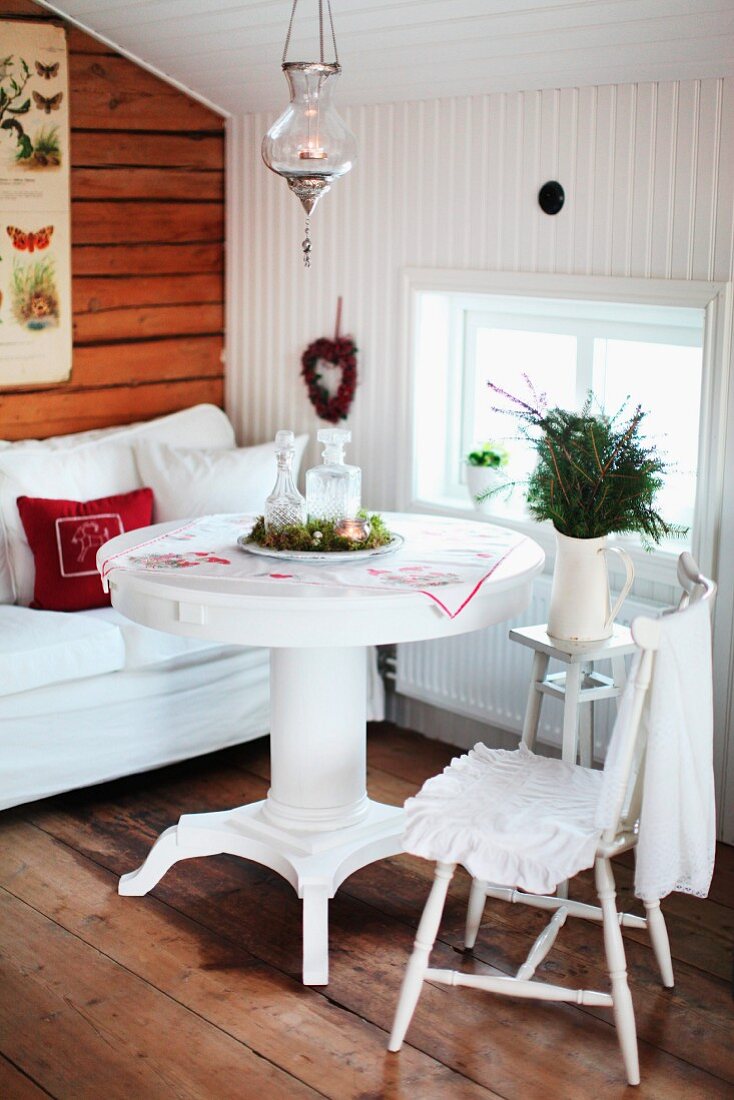Runder Esstisch und Stuhl in Weiß, Tannenzweige im Krug auf Beistelltisch vor Fenster in holzverkleidetem Dachzimmer