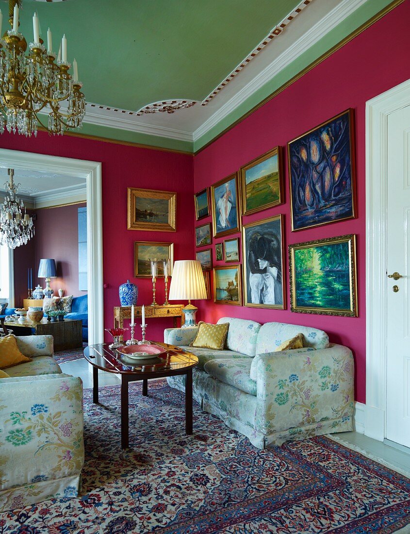 Gepolsterte Sofagarnitur mit Blumenmusterbezug in herrschaftlicher Salon Ecke, an pinkfarbener Wand Bilder mit Goldrahmen