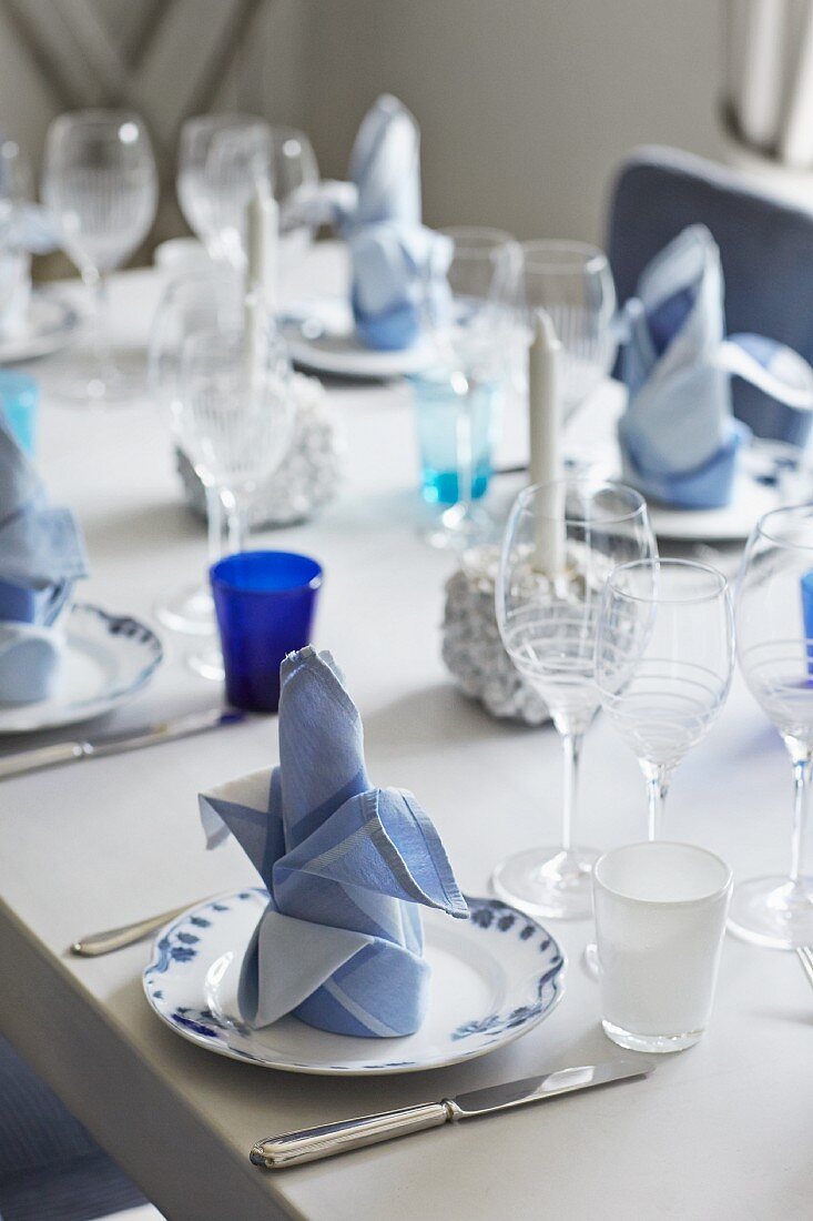 Festlich gedeckter Tisch mit weiss blauen Stoffservietten auf Teller und verschiedene Weingläser