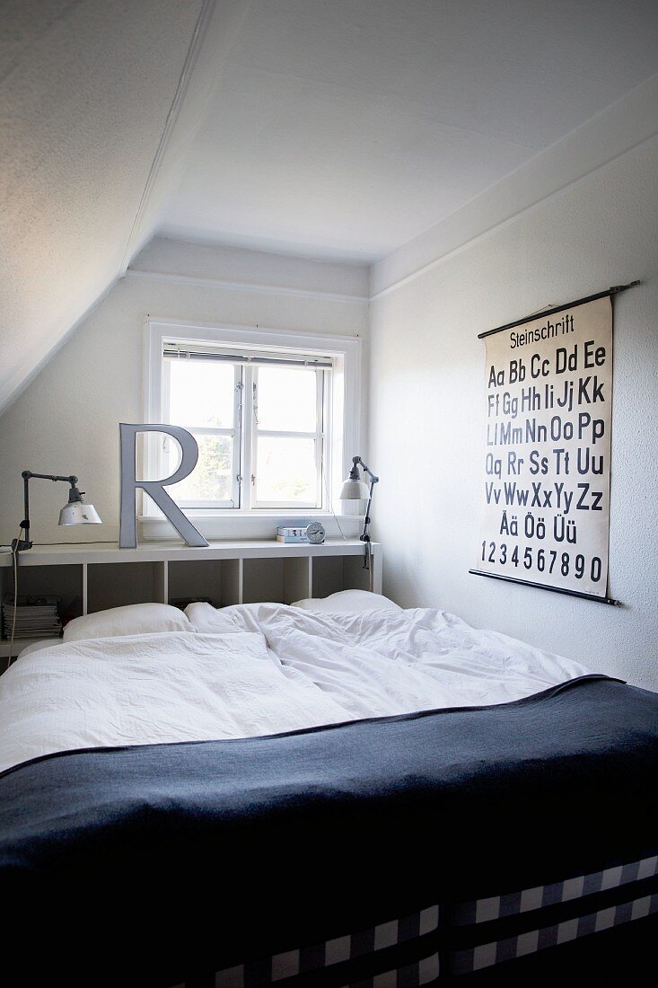 French bed with white bed linen and dark blanket in front of shelving against wall below window in attic room