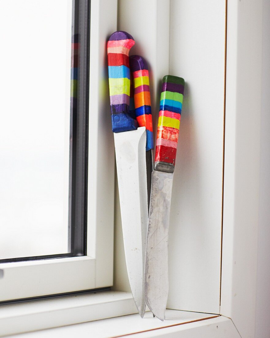 Collection of knives with handles painted in colourful stripes on windowsill