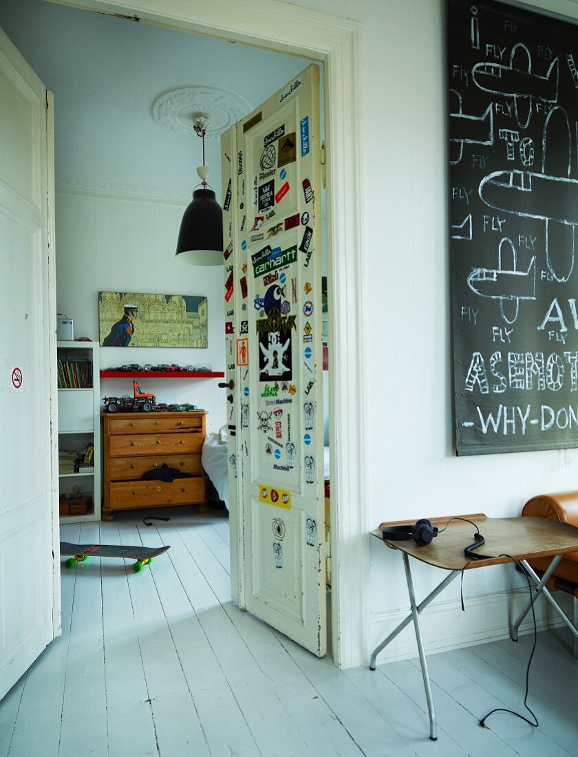 Retro folding tables next to open double doors with view into teenager's bedroom; skateboard on white wooden floor in period apartment