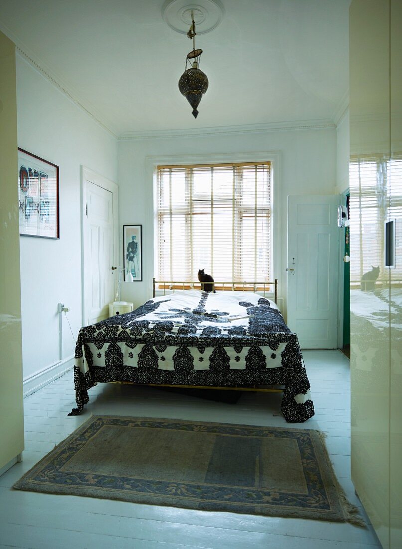 View into bedroom in minimalist, period apartment with ethnic bedspread on French bed in front of window with louvre blinds