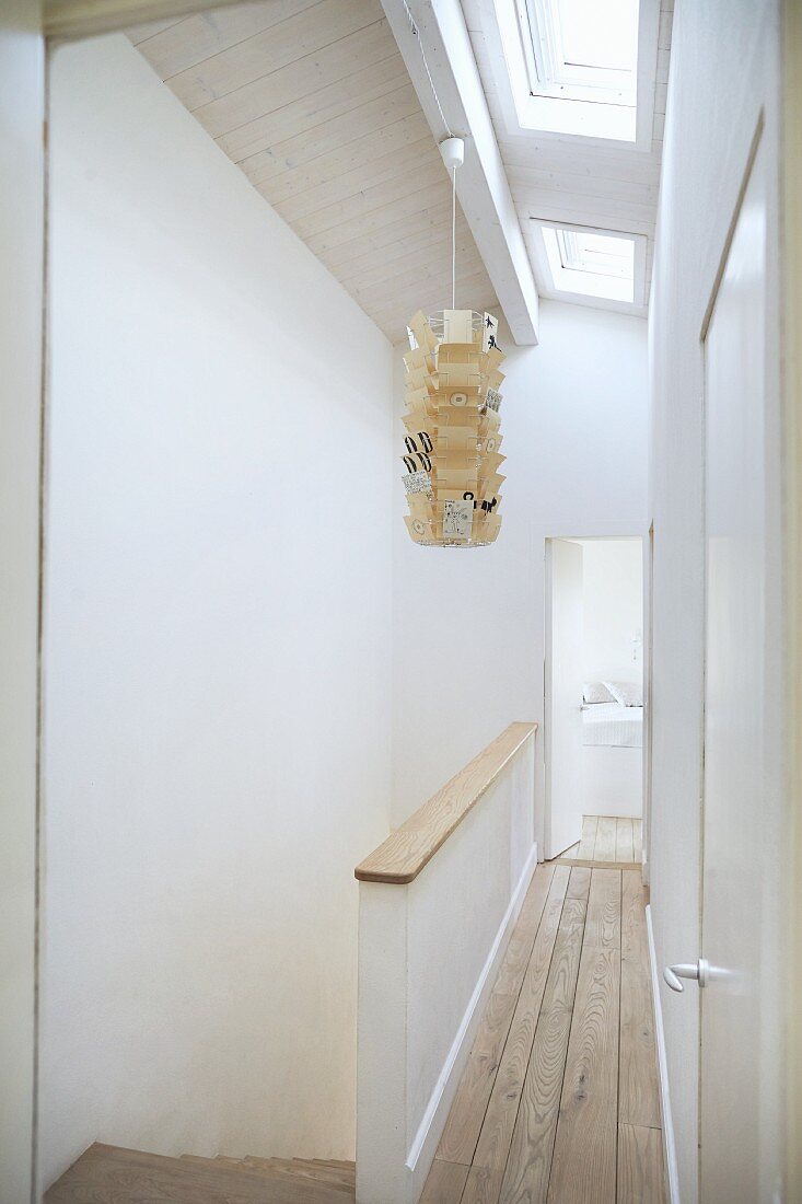 Narrow landing with wooden floor next to head of staircase and paper pendant lamp suspended from ceiling with skylights