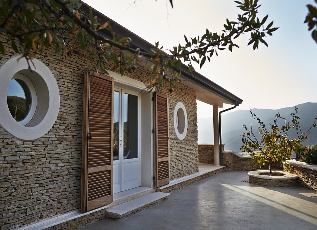 Mediterranes Wohnhaus mit Bullaugenfenster und Terrassentür mit Türläden aus Holzlamellen