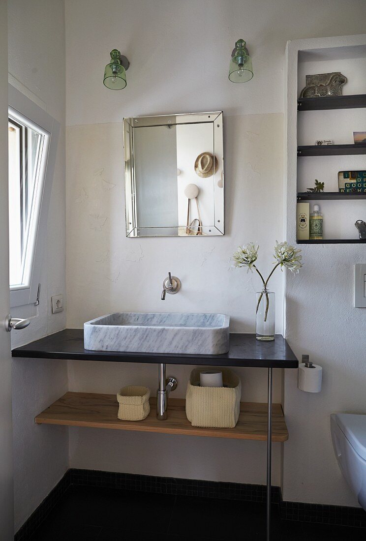 Moderner Waschtisch mit Aufbaubecken aus Marmor, darüber Spiegel und zwei Wandleuchten in Badezimmerecke