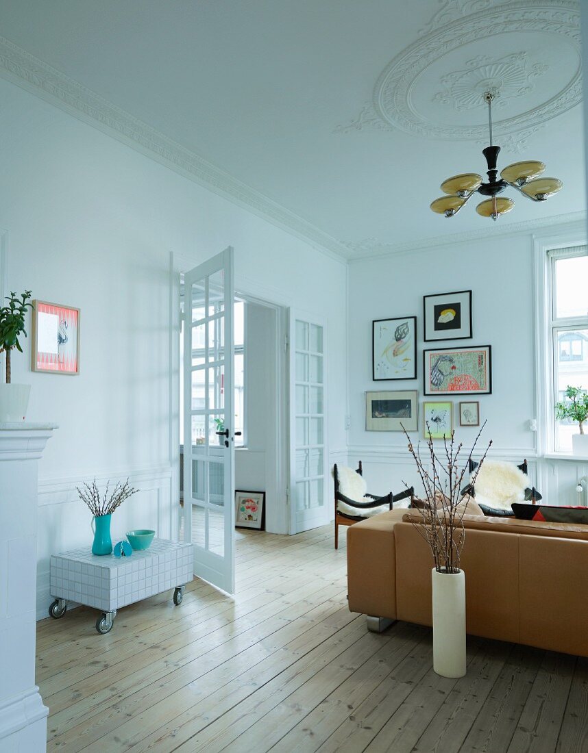 Wohnzimmer mit rustikalem Flair, Art Deco Hängeleuchte an Stuckdecke, über Sofa und Sesseln, seitlich offene Flügeltür