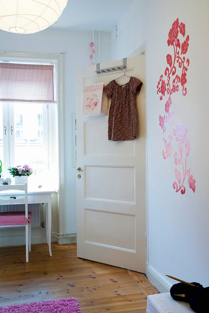 Kinderzimmer mit Blumenapplikationen an Wand, Kleidchen auf Bügel an Zimmertür gehängt