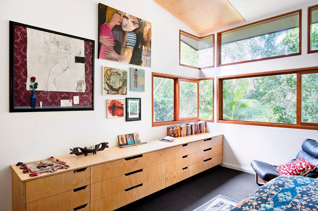 Sideboard mit Schubläden unter Zeichnungen an Wand in Schlafzimmerecke, Fensterbänder mit Aussicht in Garten