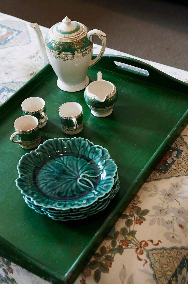 Porzellangeschirr und Blattmuster-Teller auf dunkelgrünem Holztablett