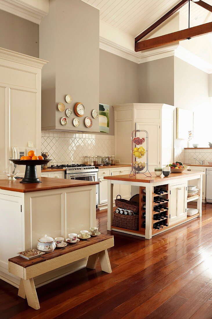 Large, open-plan country-house kitchen with wooden worksurfaces, white cabinets, white wood-clad ceiling and grey walls