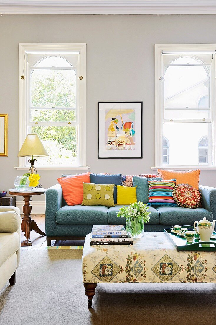 Colourful scatter cushions on blue sofa, side table and tray on ottoman in foreground