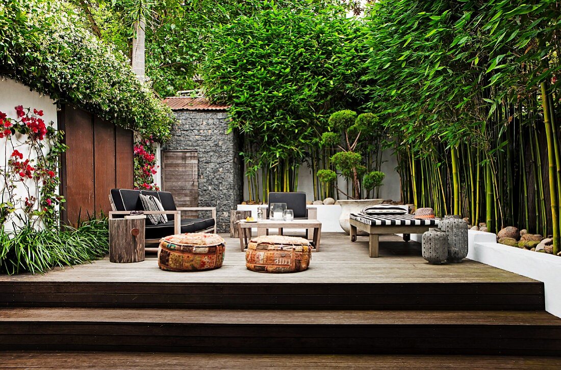 Verschiedene Terrassenmöbel auf Podest aus Holz mit Stufen im Innenhof, hochgewachsener Bambus vor Mauer