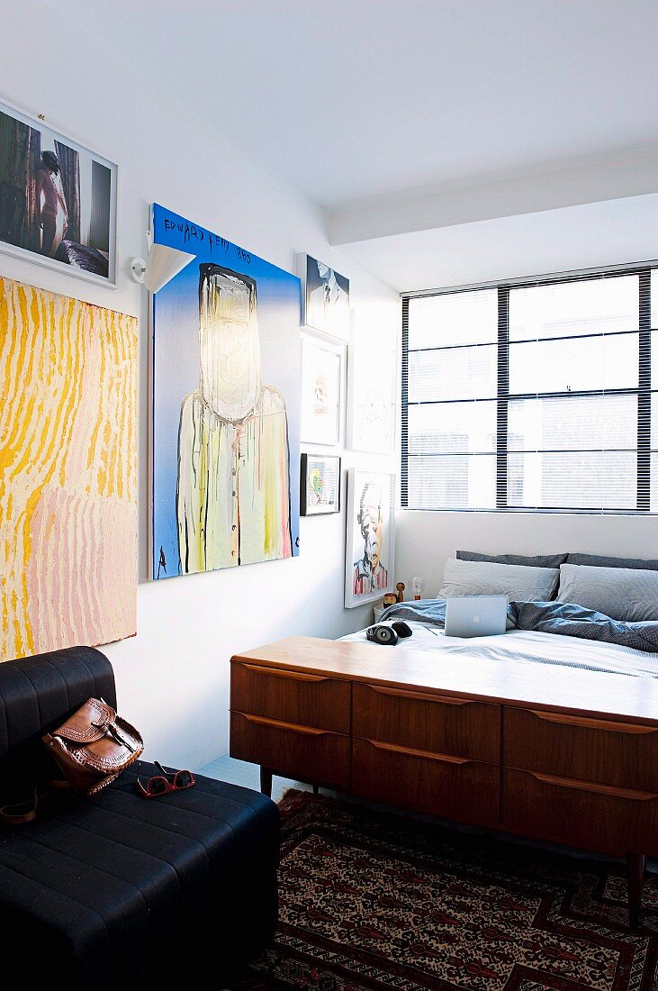 Retro Sideboard am Bettende im Schlafzimmer mit Industrie-Fenster und Kunstsammlung an der Wand