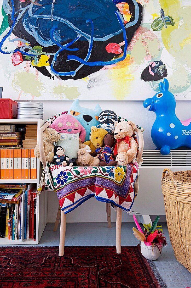 Armlehnstuhl mit Kuscheltieren, daneben Hüpftier unter farbenfroher Malerei im Kinderzimmer