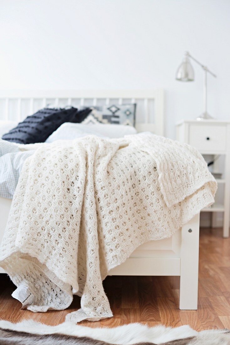 White, knitted blanket on white wooden bed in rustic room