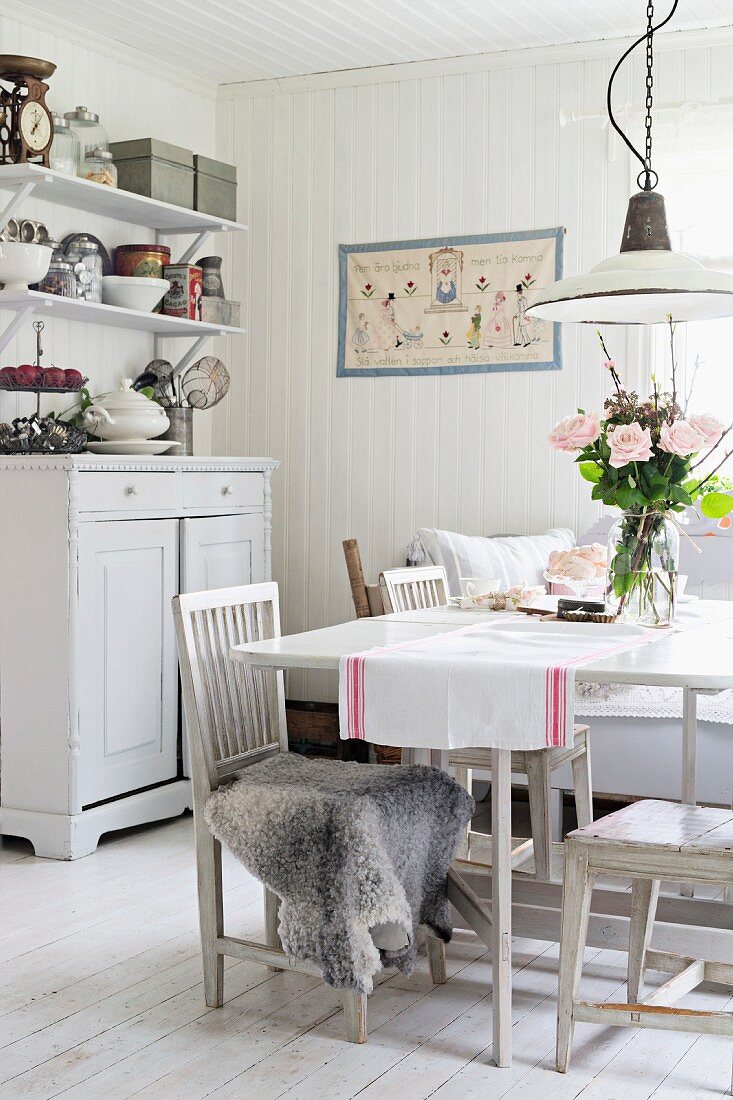Dining area with table and chairs painted white in rustic interior with white wood walls and floor