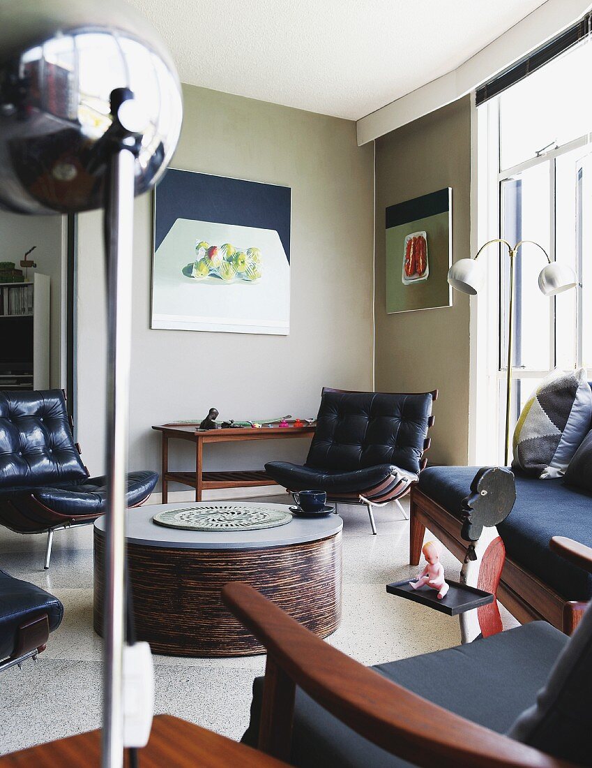 Black leather easy chairs around coffee table, retro standard lamp and modern still-life painting on wall in lounge area