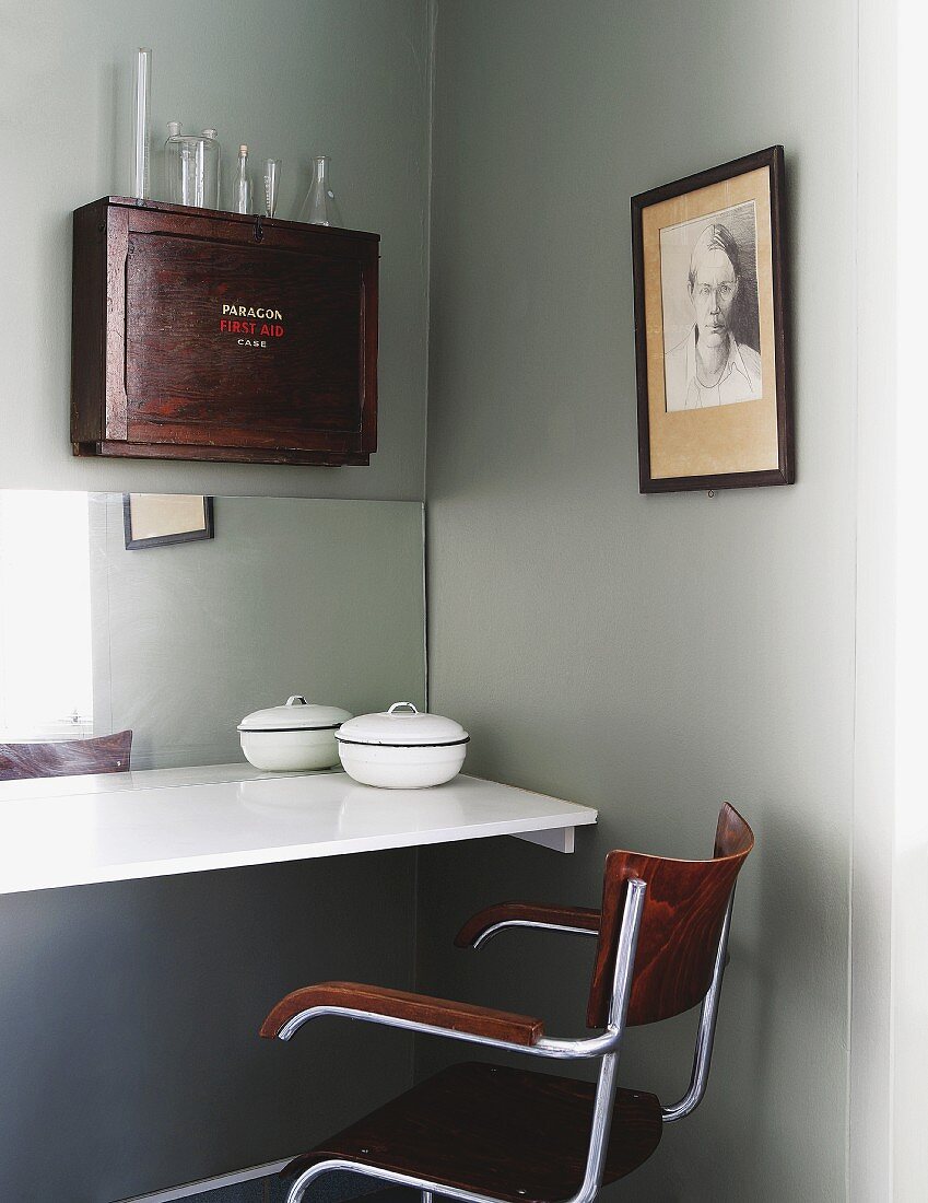 Retro-Armlehnstuhl vor an Wand montierter, weisser Tischplatte, darüber antikes Holzschränkchen