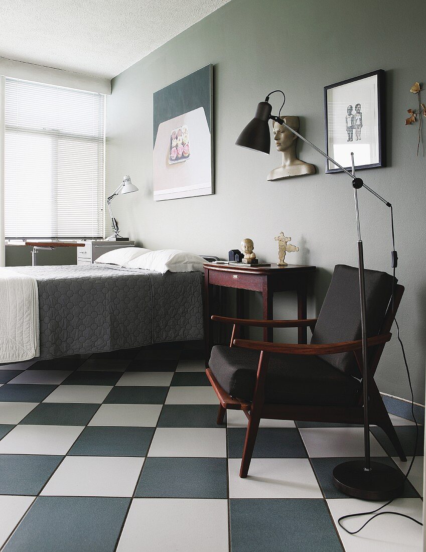 Retro-Stehleuchte neben Sessel mit schwarzem Stoffbezug im Fiftiesstil, auf Schachbrettmusterboden in grau getöntem Schlafzimmer
