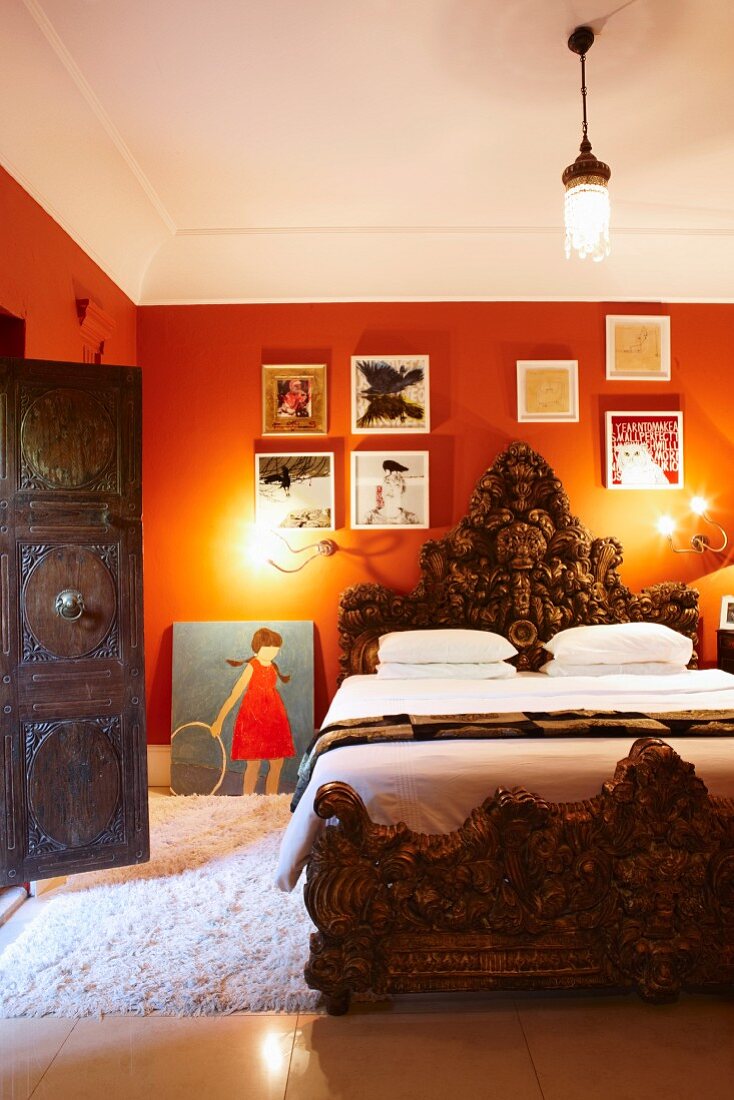 Prunkvolles Bett, Holzrahmen und Kopfteil mit üppigen Schnitzereien in traditionellem Ambiente mit orangeroten Wänden