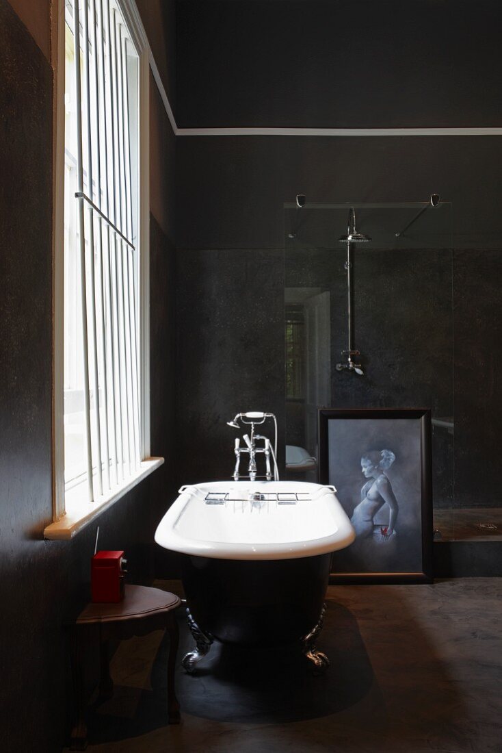 Freistehende Vintage Badewanne mit Löwenfüssen vor vergittertem Fenster in dunklem Bad