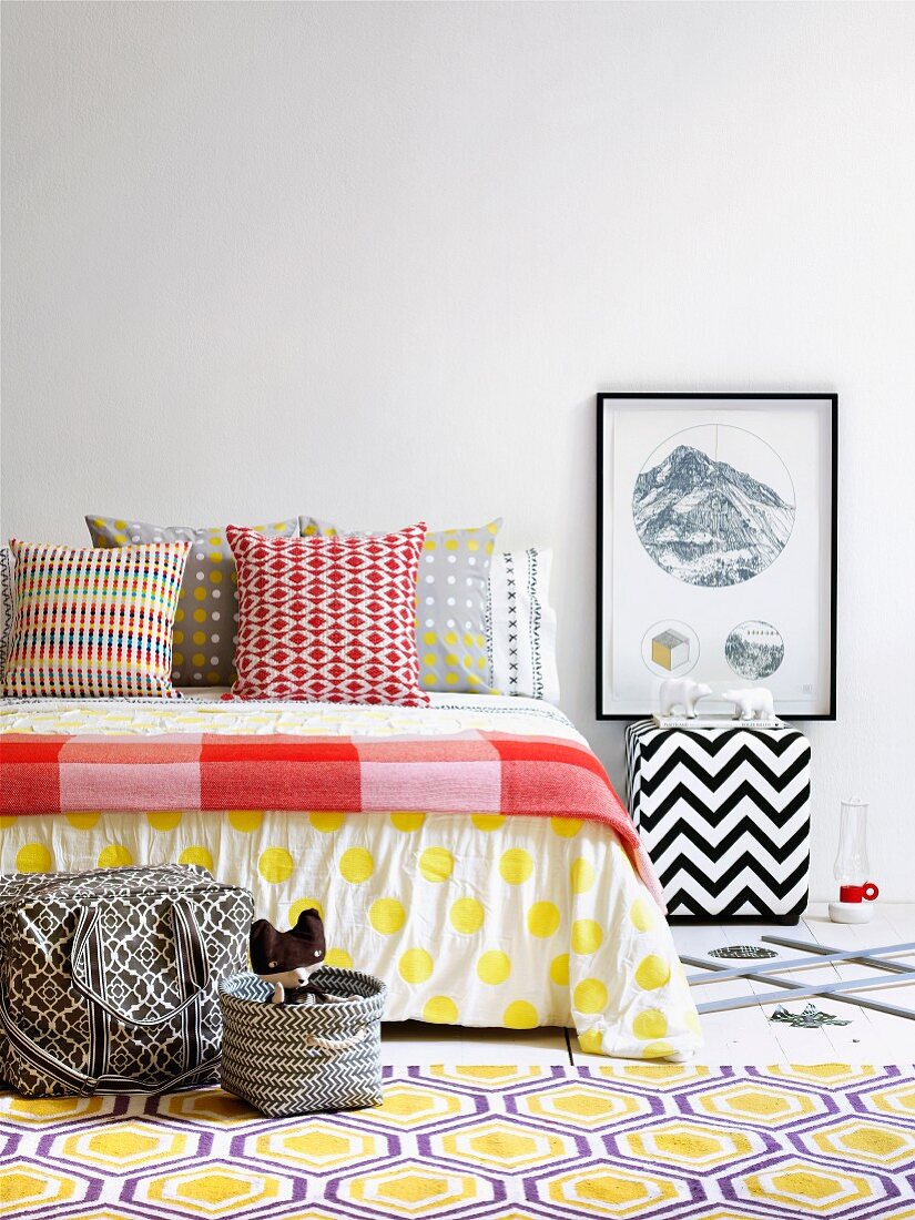 Scatter cushions in colourful mixture of graphic patterns on bed and rug with honeycomb pattern