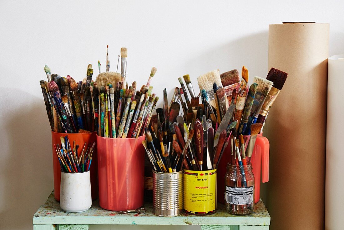 Painter's utensils - various containers of paintbrushes on cabinet next to rolls of paper
