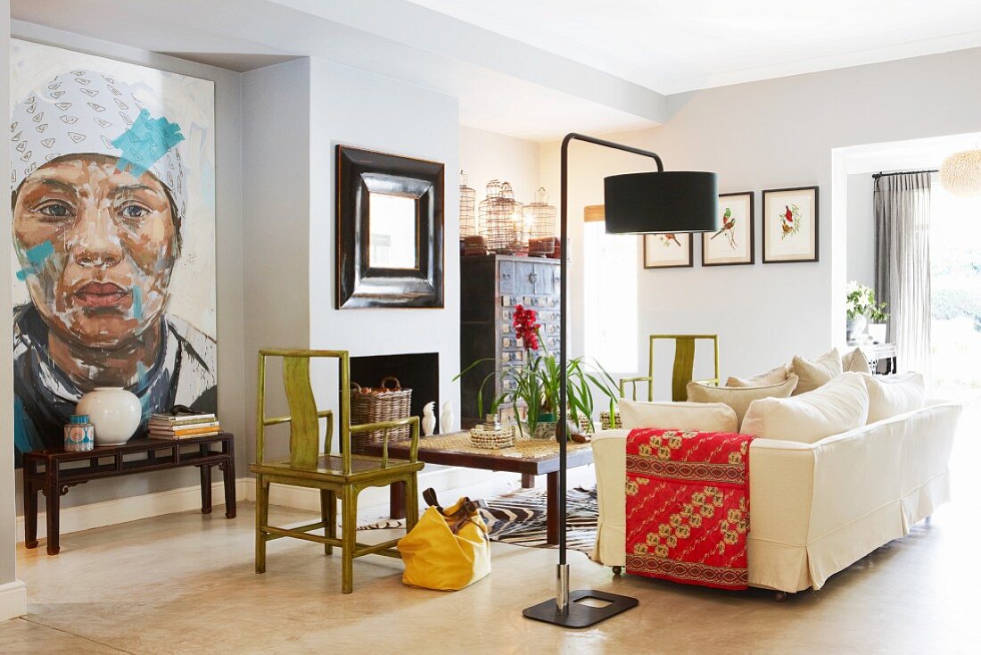 Wohnraum in eklektizistischem Stil, schwarze Retro Stehleuchte zwischen Sofa mit weisser Husse und grünen Holzstühlen, an Wand grossformtiges Portrait