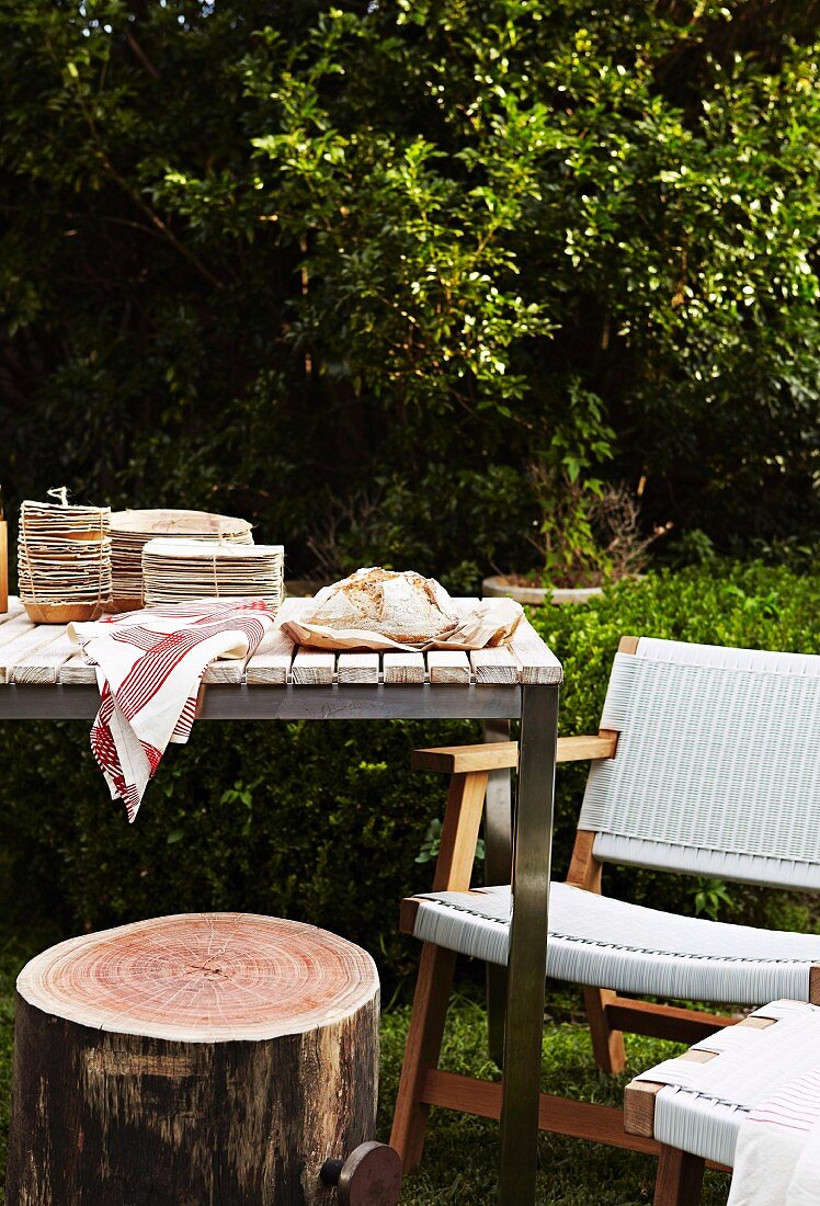 Gedeckter Tisch mit Baumstamm als Hocker und weisser Stuhl im Garten